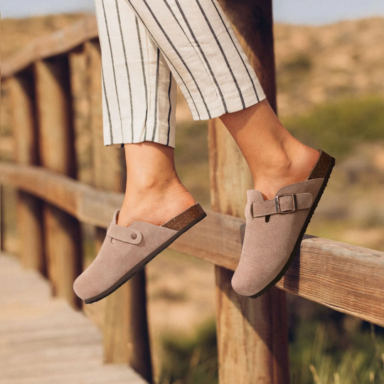 Beige orthopädische sandalen, getragen mit lässigen gestreiften hosen, ruhend auf einem sonnendurchfluteten holzgeländer